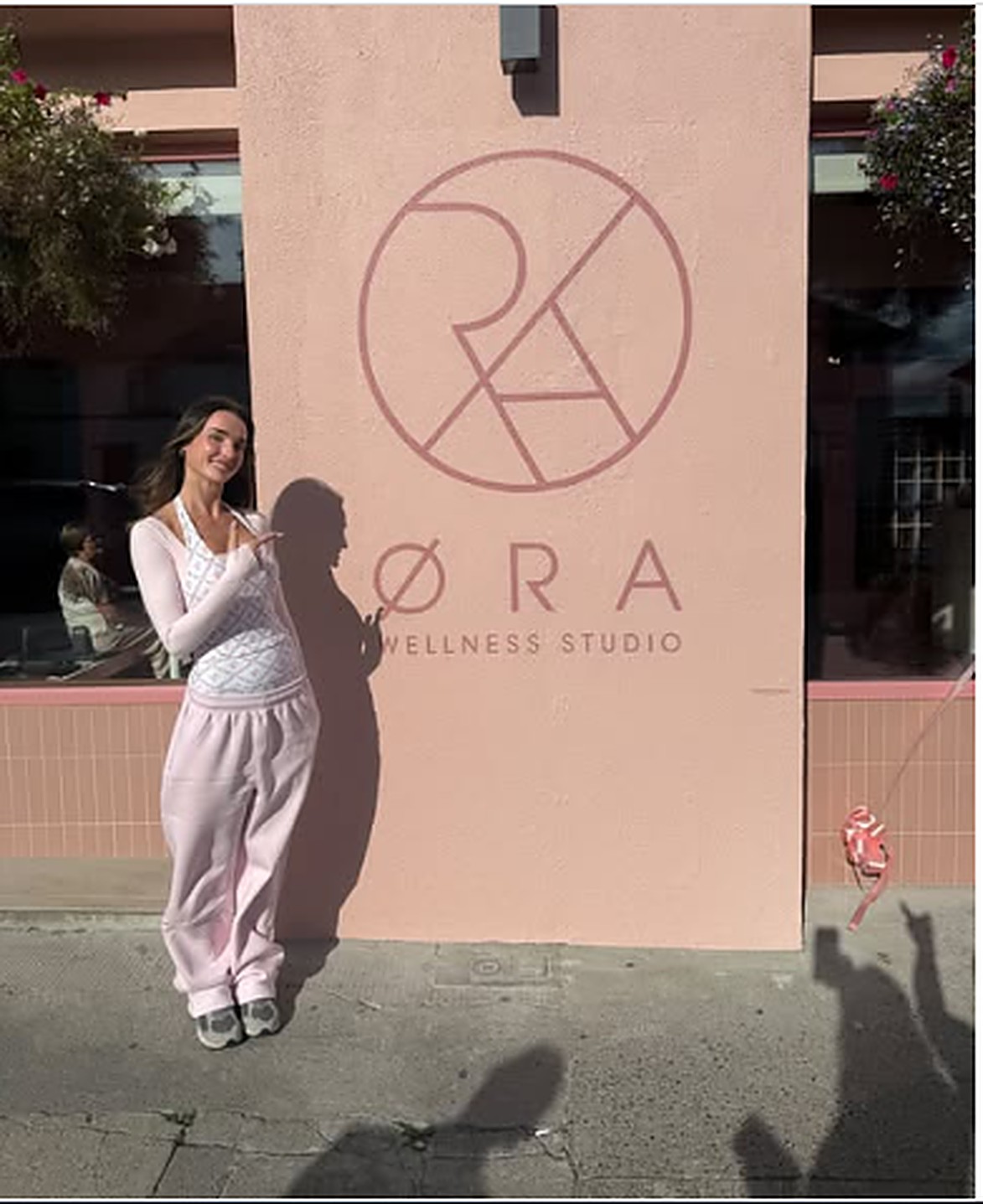 Ash pointing to the Øra Wellness Studio logo on the studio wall